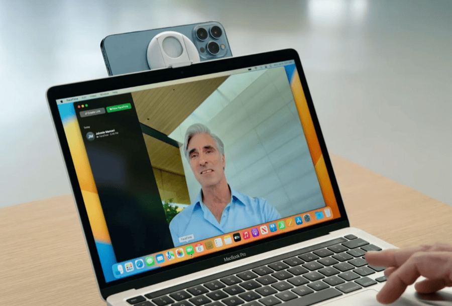 An iPhone mounted on the lid of a MacBook Pro, acting as the Mac's webcam during a FaceTime call